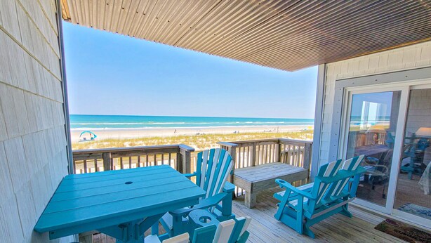Una terraza de madera con una mesa y sillas, con vista a la playa.