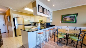 Una cocina moderna con una isla central, taburetes blancos tipo barra, una mesa de comedor con sillas y obras de arte enmarcadas en las paredes.