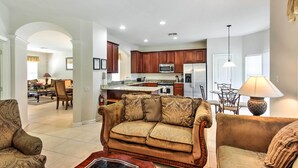 A spacious living room with a large sofa and a coffee table, a kitchen with wooden cabinets and modern appliances, and a dining area with a table and chairs. - Spacious Kissimmee Villa - 3 Mi to Disney World! (Kissimmee)