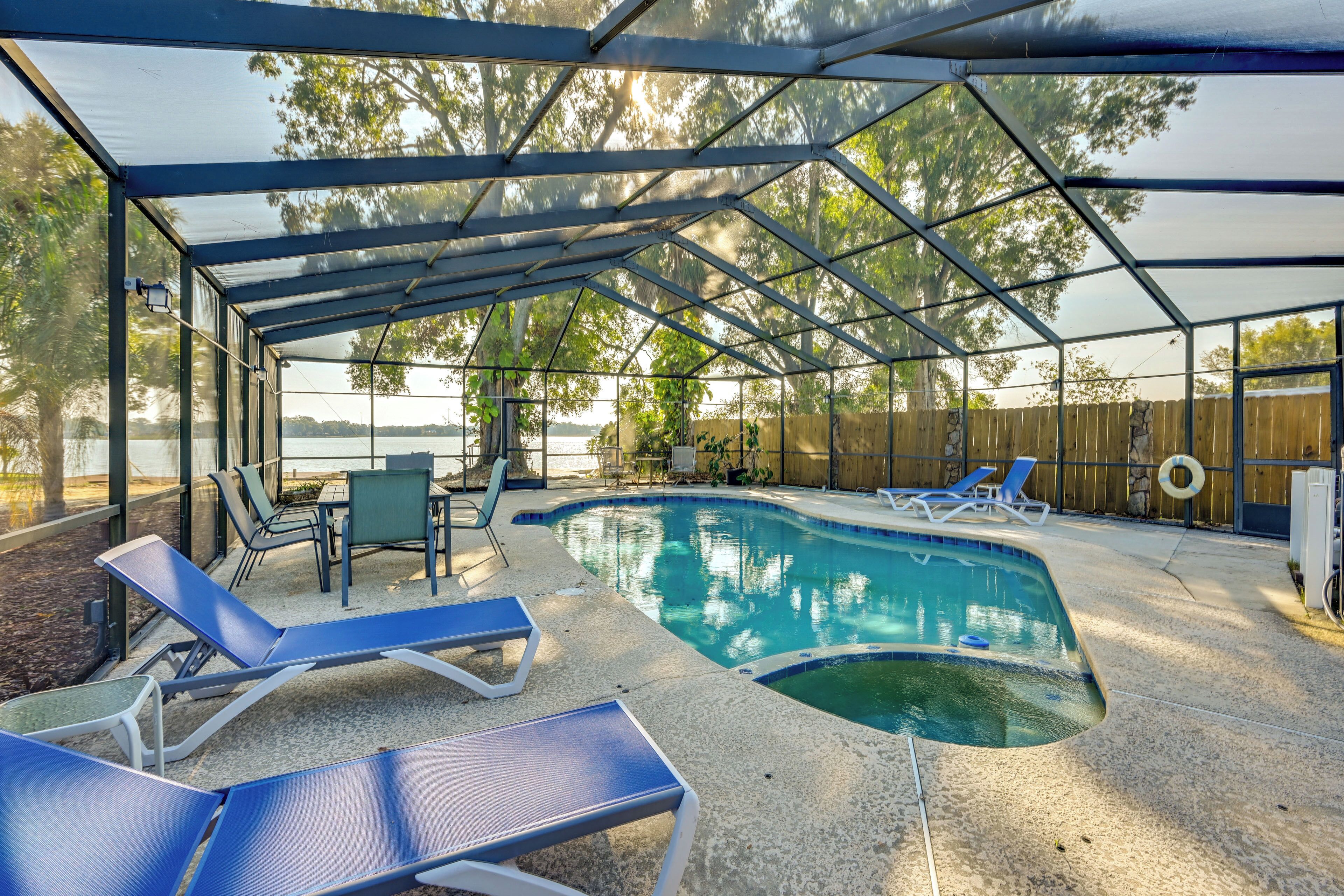 Une piscine extérieure couverte, dotée de chaises longues et d’une table, et entourée d’une clôture en bois et d’arbres.