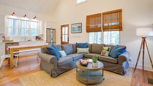 A spacious living area with a large sectional sofa, a round coffee table, and a dining table with benches. There are large windows with blinds, a refrigerator, and a lamp. - Enchanting Andersonville Home Steps to Norris Lake (Andersonville)