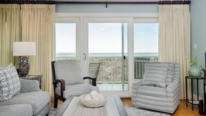 A living room with a sofa, armchairs, a coffee table, and a view of the sea through large glass doors. - Upgraded Oceanfront 3BR Condo in WrightsvilleDunes (Wrightsville Beach)