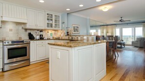A spacious kitchen with white cabinetry, a large island, and a dining area with a view. - Upgraded Oceanfront 3BR Condo in WrightsvilleDunes (Wrightsville Beach)