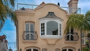 A two-story building with a bay window, balconies, and a small garden area. - Beautiful, bright and charming 3-story townhouse on an amazing street in Newport! (Newport Beach)