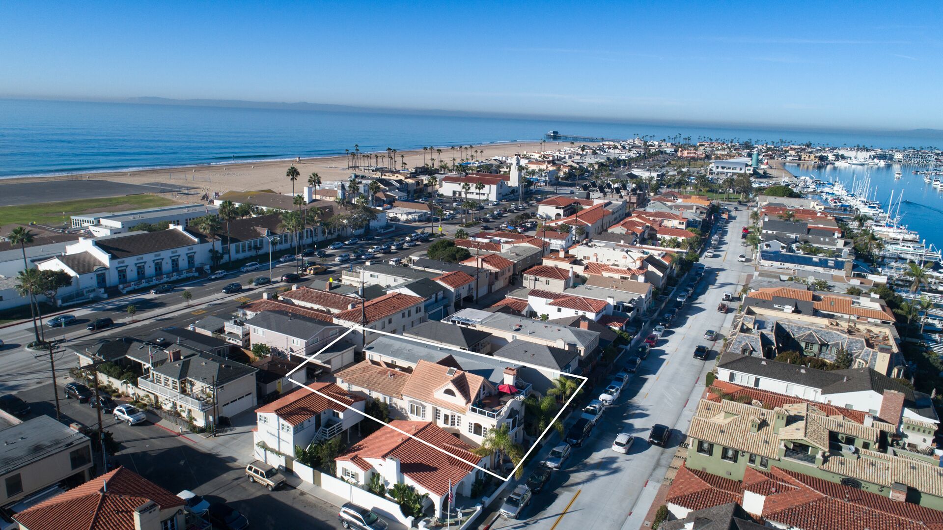 Vista aérea de uma cidade costeira com um porto de iates, edifícios residenciais e uma praia.