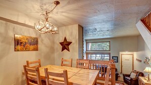 Un comedor con una mesa y sillas de madera, una araña, un adorno con forma de estrella y un cuadro de árboles.