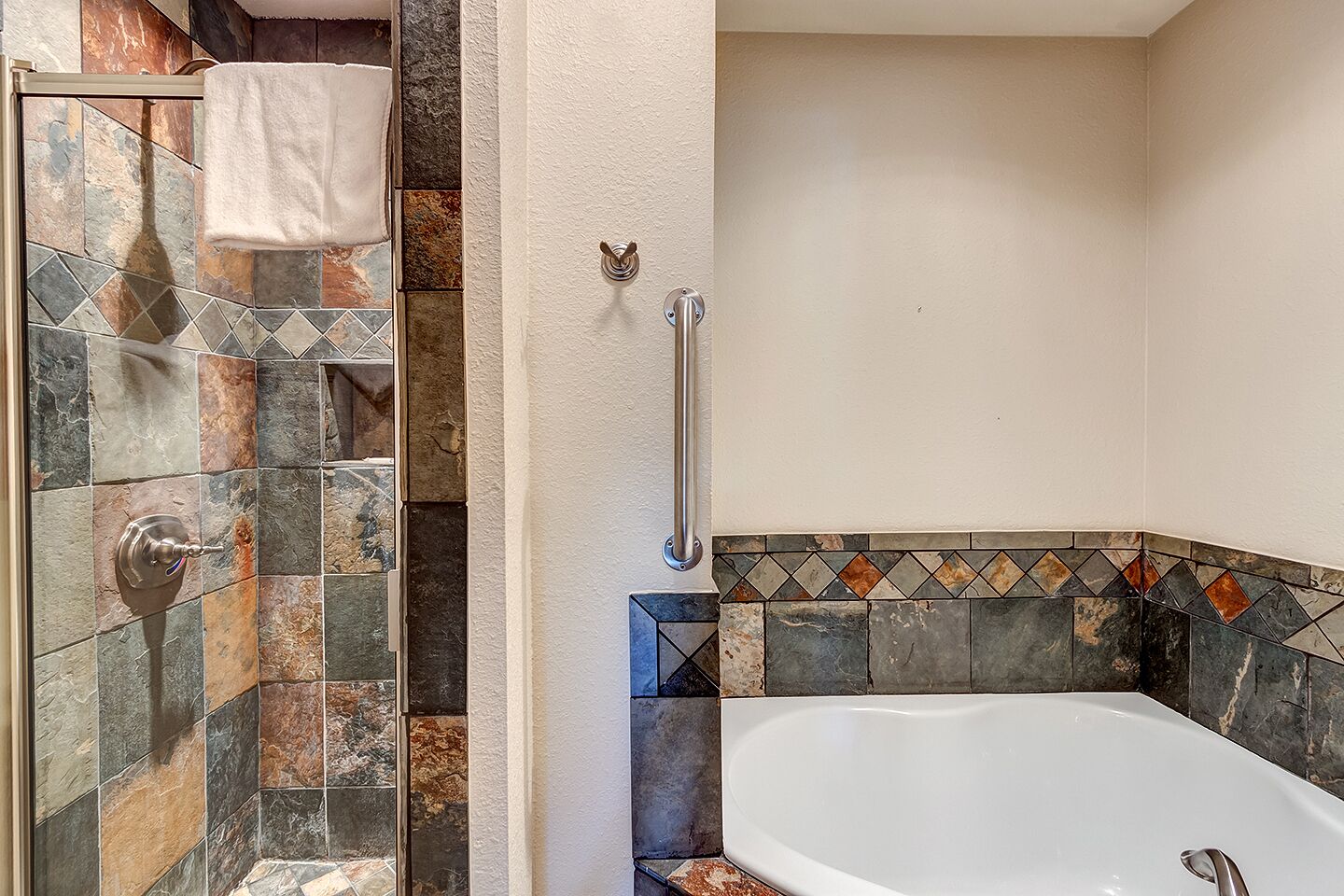 A bathroom with a shower, a bathtub, and a handrail.