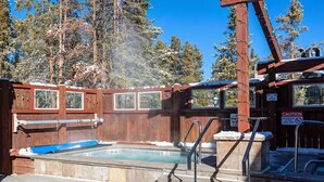 Zona de hidromasaje con terraza de madera, escalones de piedra y un letrero de precaución sobre la prohibición de fumar.