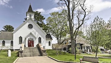 Une église blanche avec une porte rouge et un clocher, entourée d’arbres et d’un banc.