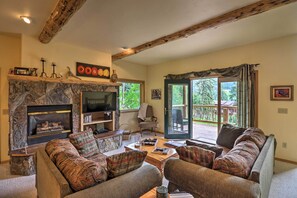 A cozy living room with a stone fireplace, comfortable seating, and a large window offering a view of the outdoors. - Rustic Home on Whitefish Mountain, Near Ski Run! (Whitefish)