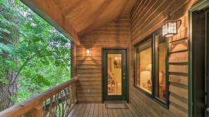 A wooden porch with a railing, a door leading inside, and a view of the surrounding trees. - Rustic Home on Whitefish Mountain, Near Ski Run! (Whitefish)