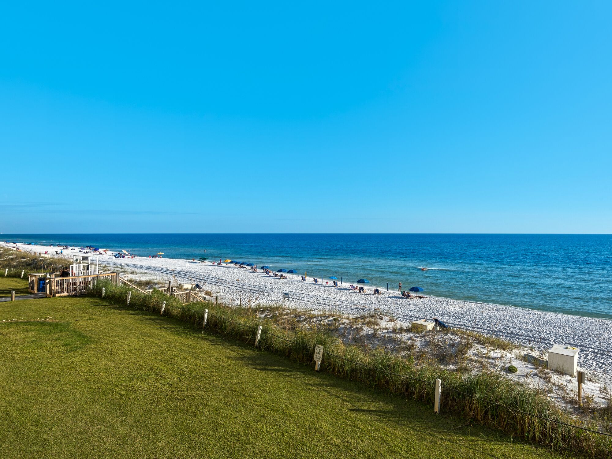 A beach with a wooden walkway leading to the shore, a grassy area in the foreground, and the ocean in the background.