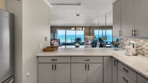 A modern kitchen with grey cabinets, a large island, and a view of the ocean. - Beach House Condominium 202B by Newman-Dailey (Miramar Beach)