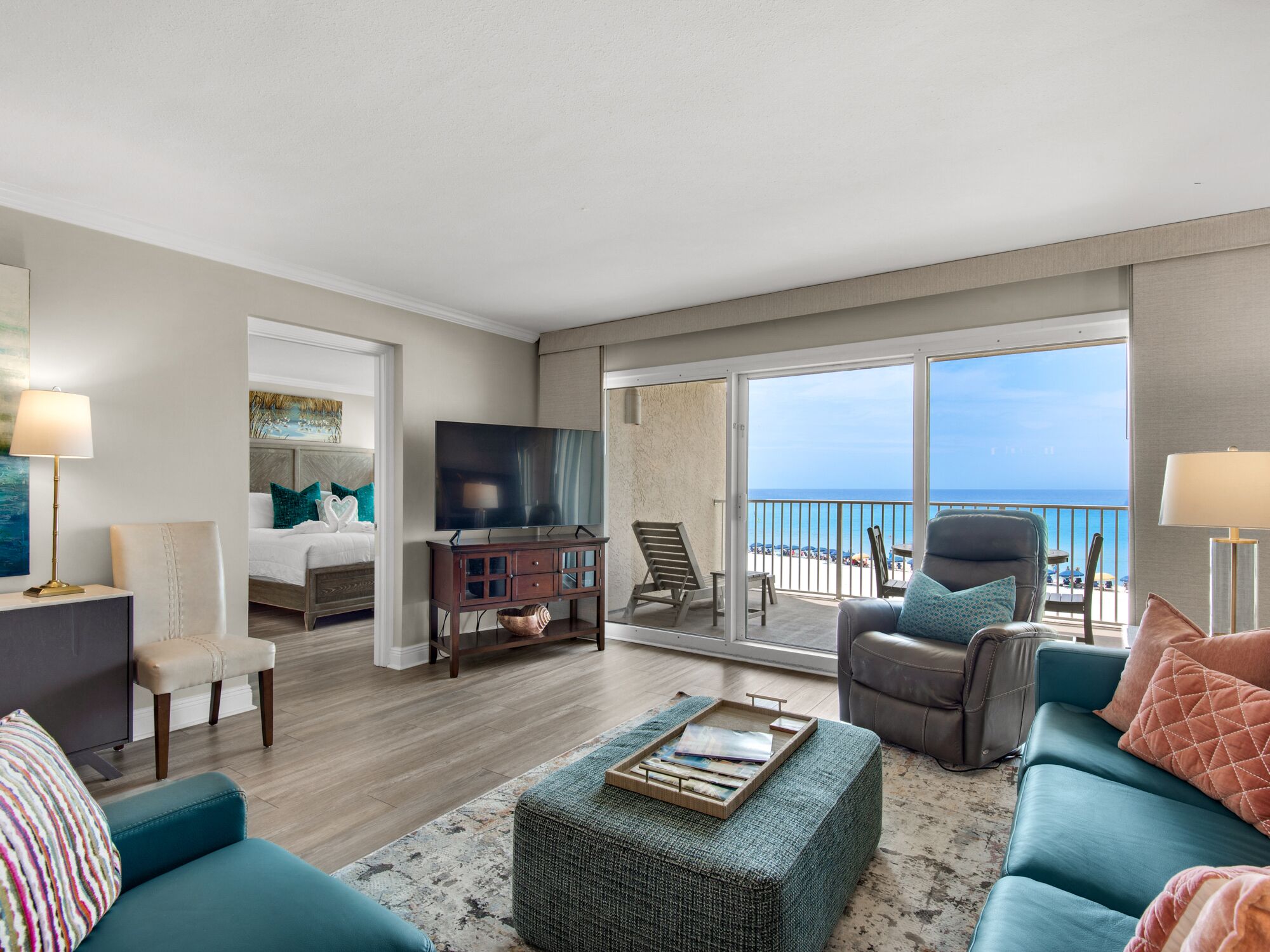 A spacious living room with a large window overlooking the beach, a comfortable sofa, a television, and a dining area.
