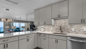 A modern kitchen with grey cabinets, a stainless steel sink, and a tiled backsplash. - Beach House Condominium 202B by Newman-Dailey (Miramar Beach)