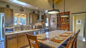 A modern kitchen with wooden cabinets, a large island, and a dining area set for six. - Hidden Santa Fe Gem - Nestled in Tesuque Hills! (Santa Fe)