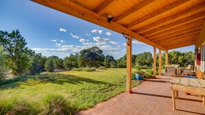A covered patio with a brick floor, wooden furniture, and a view of a grassy yard and trees. - Hidden Santa Fe Gem - Nestled in Tesuque Hills! (Santa Fe)