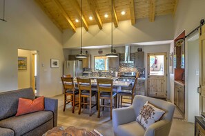 A spacious living area with a kitchen in the background, wooden ceiling beams, and a dining area with chairs and a table. - Hidden Santa Fe Gem - Nestled in Tesuque Hills! (Santa Fe)