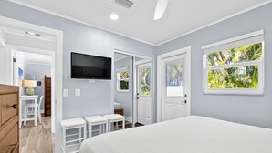 Quarto com cama, televisão, escrivaninha e janela com vista para o verde.