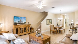 A living room with a sofa, coffee table, and a TV. There's a staircase leading to another room. - Storey Lake Resort home with Mini-Golf & Lazy River | Private Pool | Sleeps 10 (Kissimmee)