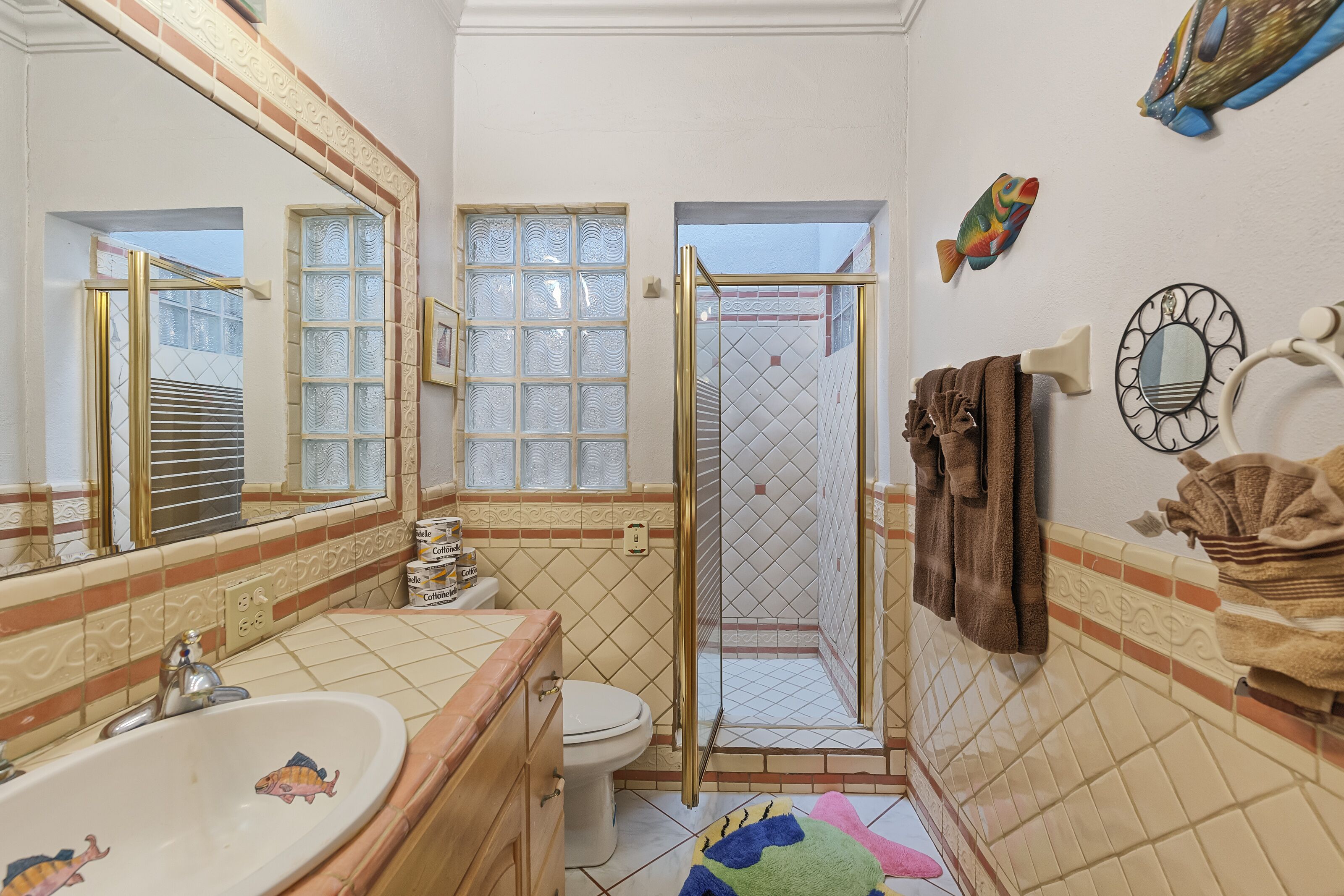Une salle de bain équipée d’un lavabo, de toilettes, d’une douche et décorée avec un motif de poissons sur le mur.