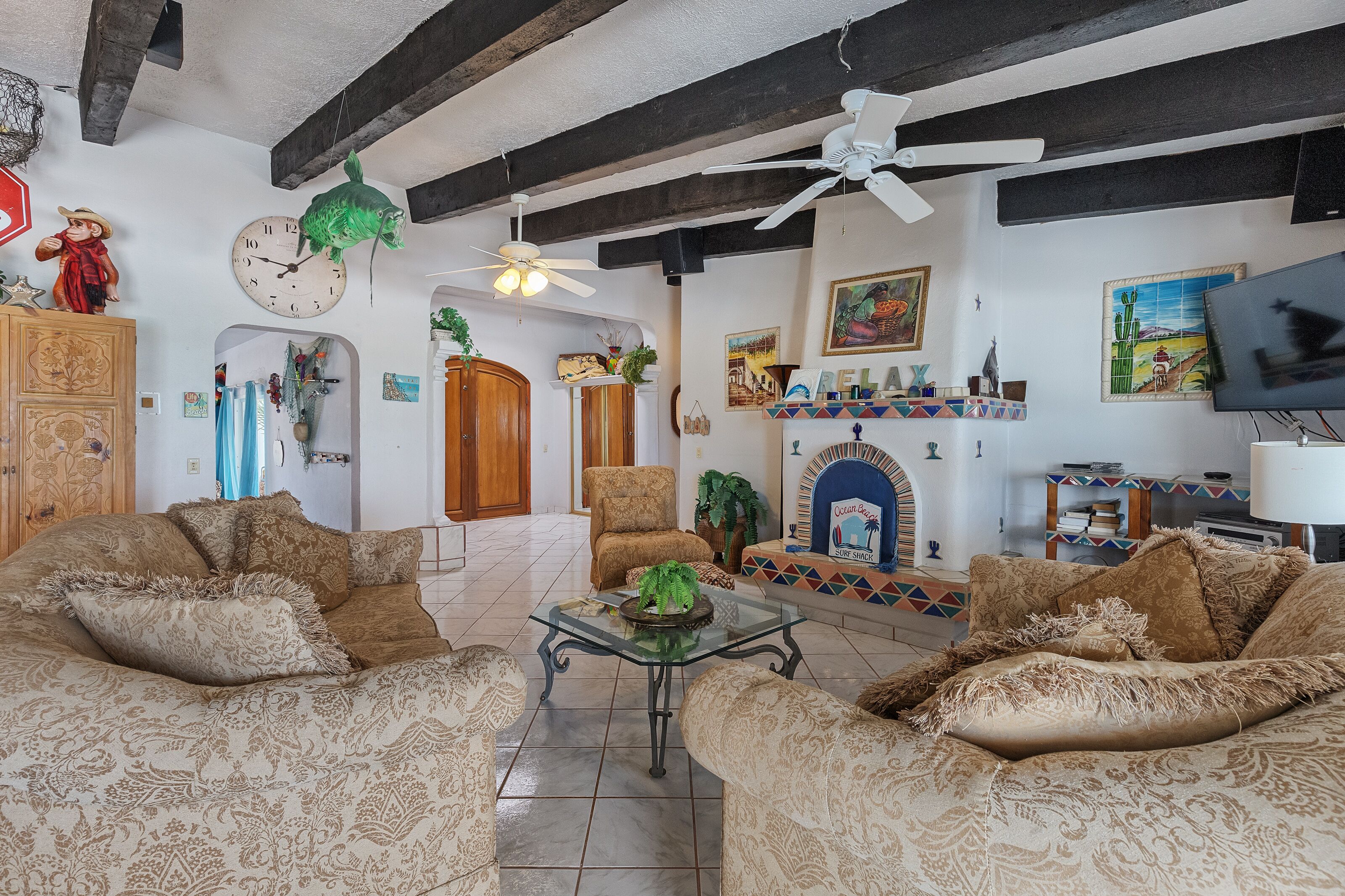 A living room with two patterned sofas, a glass coffee table, a fireplace, and various wall decorations.