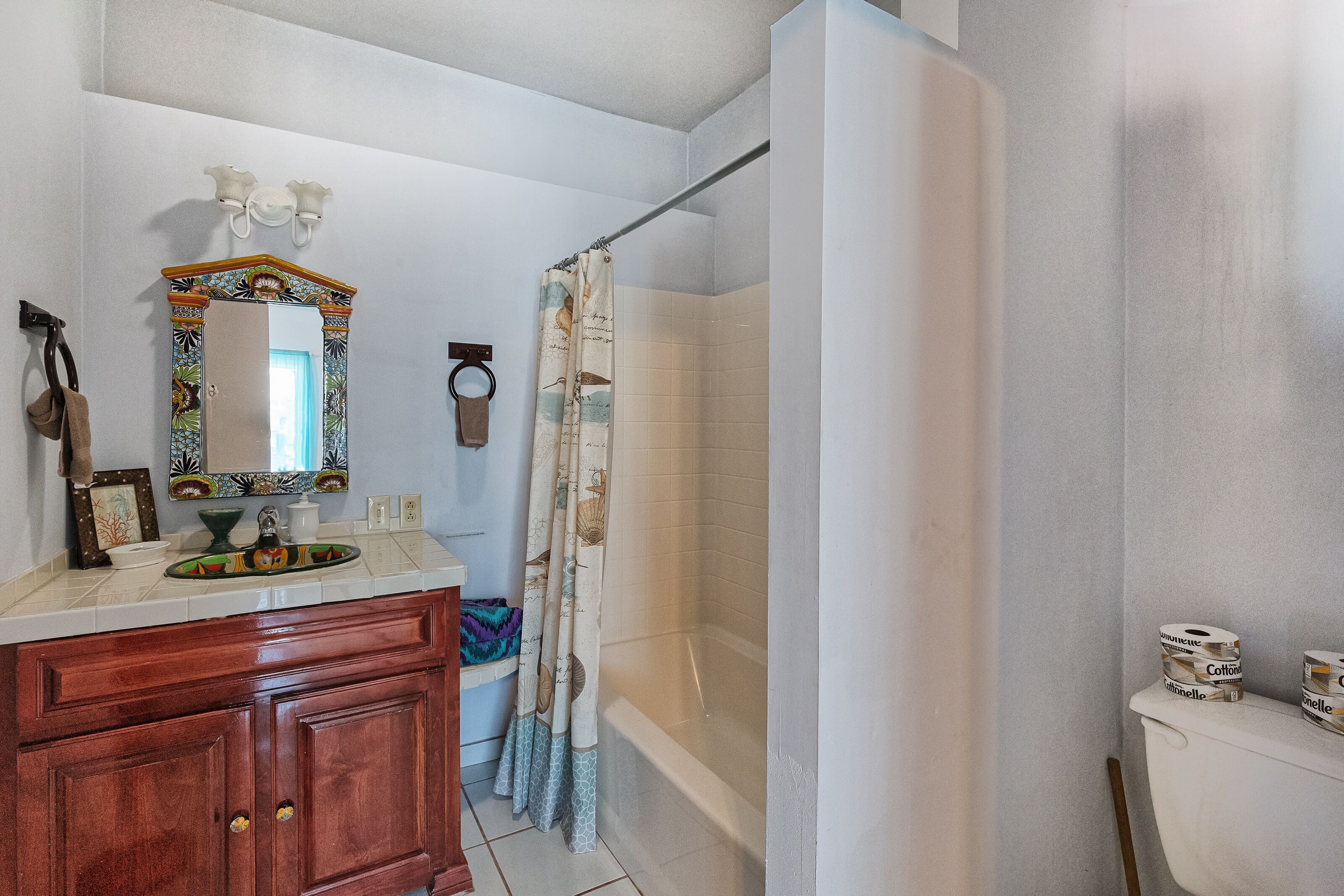 Une salle de bain avec un meuble-lavabo en bois, un miroir avec un cadre décoratif, une douche avec un rideau et des toilettes avec du papier toilette.