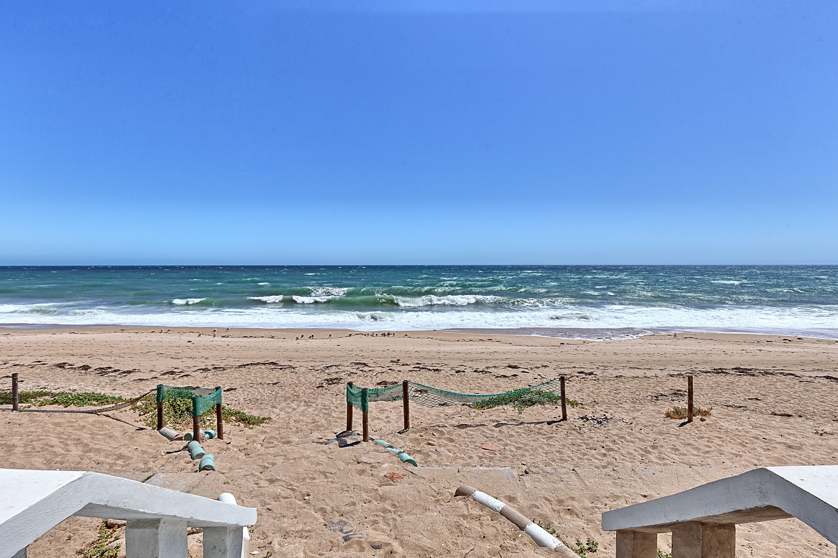 Una platja amb una zona delimitada per una xarxa i una estructura de fusta en primer pla.