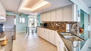 A modern kitchen with white cabinets, a tiled backsplash, and a stainless steel sink. - Waterfront Getaway w/ Pool & Dock - Walk to Beach! (Indian Rocks Beach)