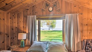 Une chambre à coucher dans une cabane en bois, avec un lit, une table de chevet, une lampe et une vue sur un champ verdoyant.