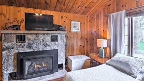 Une chambre confortable dans un chalet, avec une cheminée en pierre, une télévision et un lit donnant sur une fenêtre avec vue.
