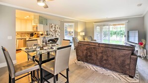 A modern living room with a brown sofa, a glass dining table, and a ceiling fan. - Pool & Hot Tub Access: Modern Palm Springs Condo (Palm Springs)
