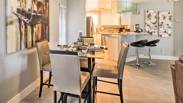 A modern dining area with a glass table, chairs, and a ceiling fan. A kitchen is visible in the background with a refrigerator and cabinets. - Pool & Hot Tub Access: Modern Palm Springs Condo (Palm Springs)