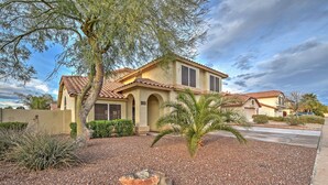 A two-story house with a tiled roof, a landscaped front yard with a palm tree, and a clear sky. - Hot Tub & Pool: Stunning Goodyear Home Near Lakes (Goodyear)