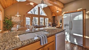 A kitchen with granite countertops, a stainless steel refrigerator, wooden cabinets, and a stone fireplace. - Waterfront Grand Lake House w/ Dock & Kayaks! (Eucha)