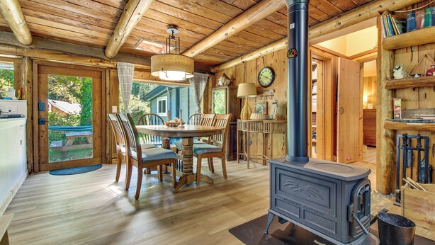 A wooden interior with a dining table, chairs, a stove, and a bookshelf. - Hike to the Coast! Log Cabin on 5 Acres in Bandon (Bandon)