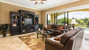 A living room with a fireplace, a large TV, a sofa, and a view of a pool. - Radiant Retreat with Golf Course Views at Reunion (Kissimmee)