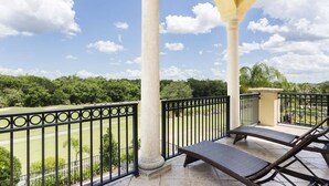 A balcony with two lounge chairs, a view of a golf course, and a clear sky. - Radiant Retreat with Golf Course Views at Reunion (Kissimmee)