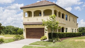 A two-story house with a brown garage door, a covered patio, and a well-maintained lawn. - Radiant Retreat with Golf Course Views at Reunion (Kissimmee)