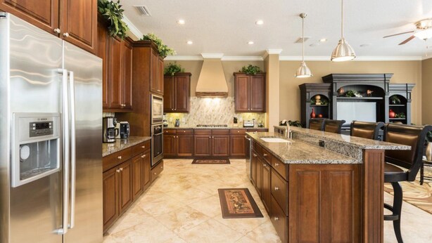 A spacious kitchen with wooden cabinets, a stainless steel refrigerator, a granite countertop island, and a built-in oven. - Radiant Retreat with Golf Course Views at Reunion (Kissimmee)