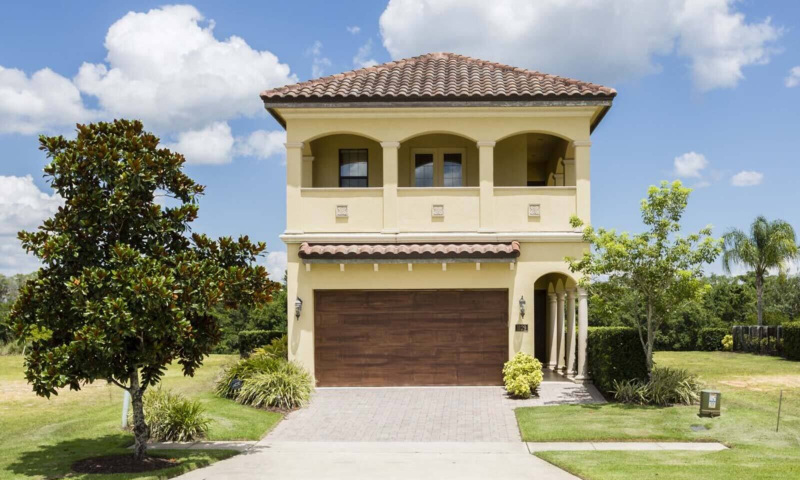 A two-story house with a brown roof, beige walls, and a large garage door.