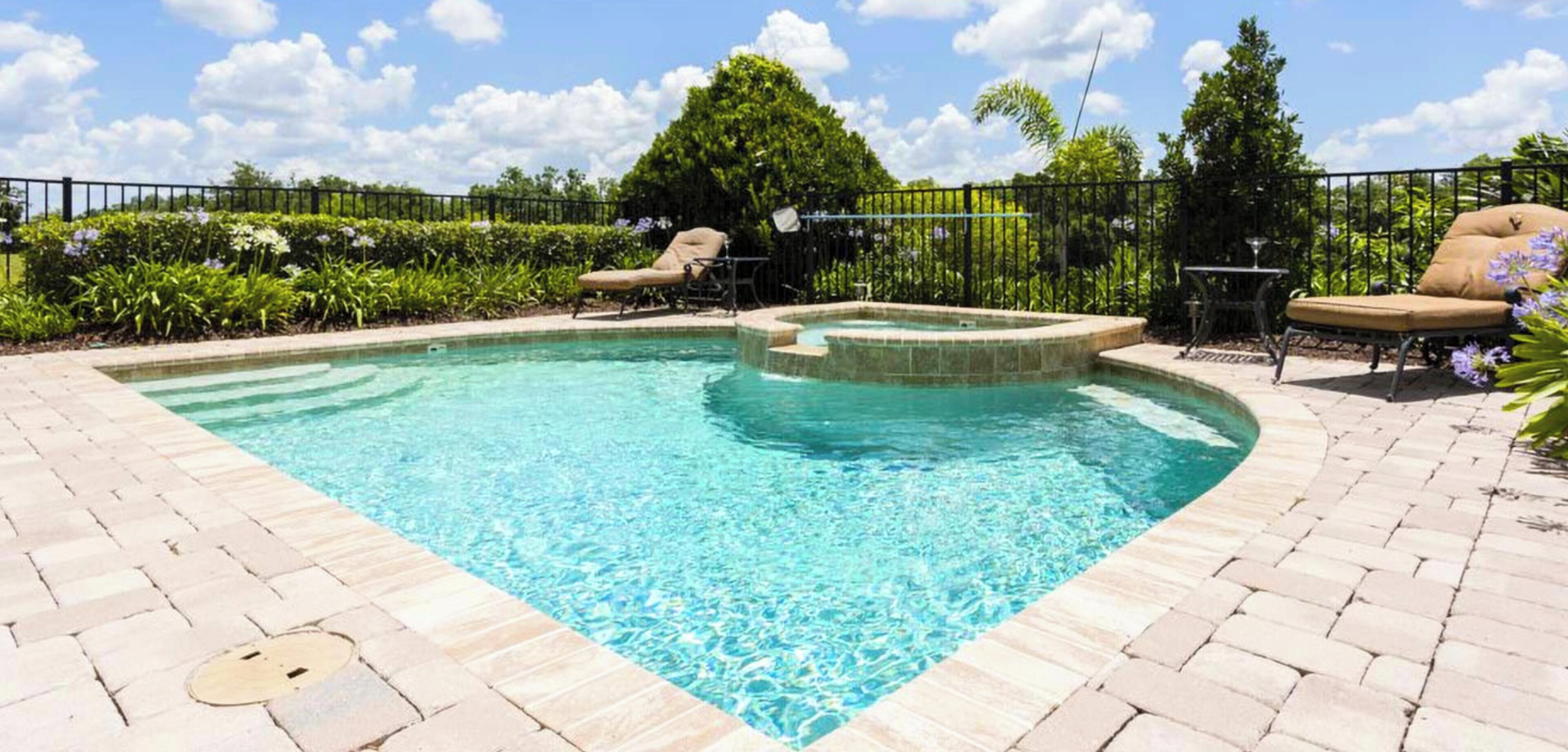 A swimming pool with a hot tub, surrounded by a brick patio and a metal fence.