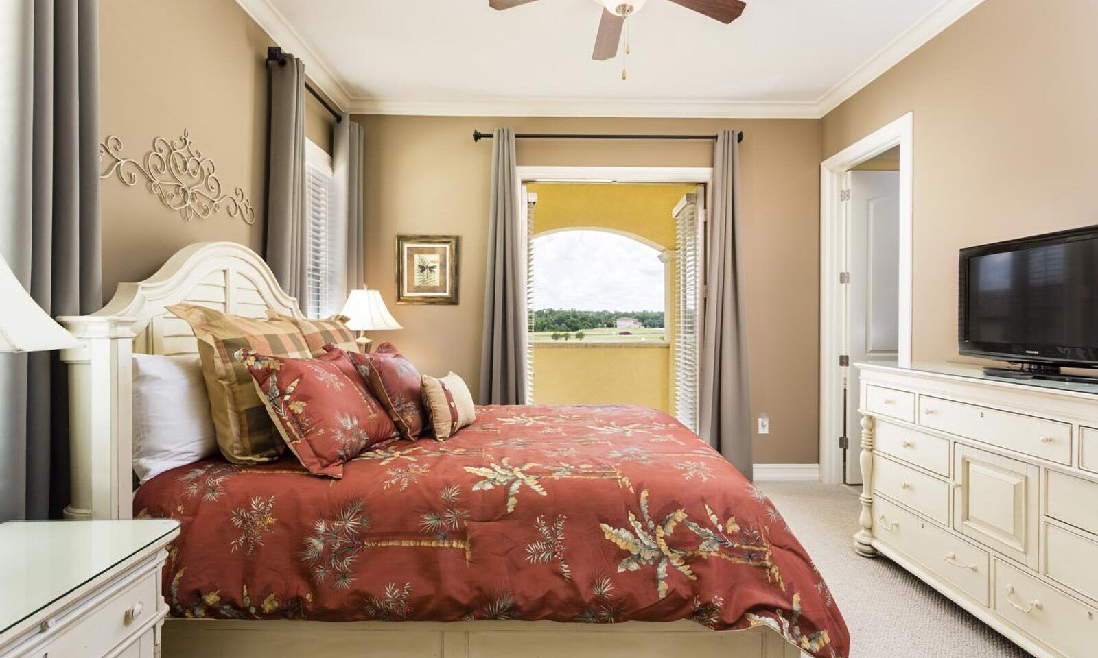 A bedroom with a bed, a television, a dresser, and a window with curtains.