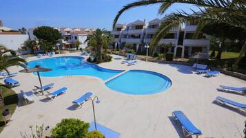A resort with a large swimming pool, sun loungers, and palm trees.