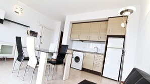 Una cocina moderna con lavadora integrada, un comedor con mesa de vidrio y un sofá negro.