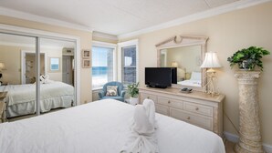 A hotel room with a large bed, a television, a dresser, a mirror, and a potted plant.