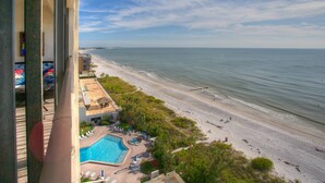 A beach view from a balcony with a swimming pool and lounge chairs. - Views from Beachfront Balcony ~ Pool ~ Updated    Fantastic Location Near Shops Bars and Restaurants (Madeira Beach)