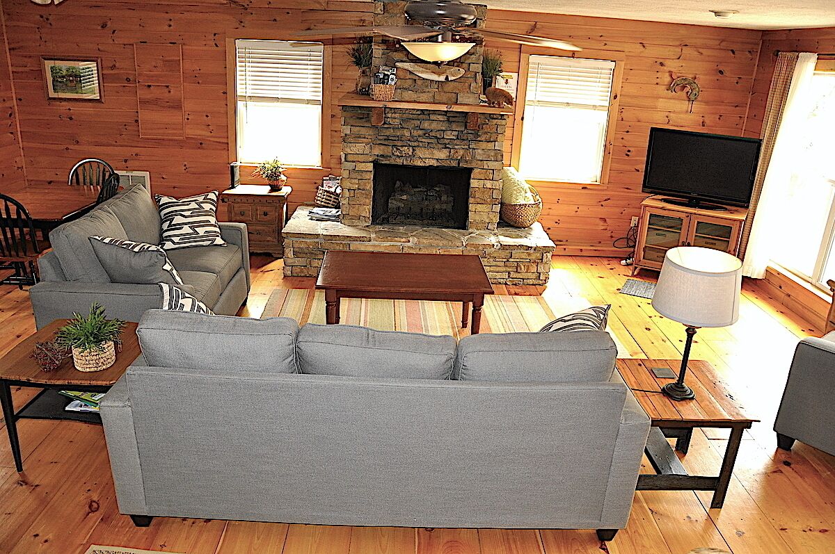 L’intérieur d’un chalet confortable, avec une cheminée en pierre, un canapé gris, un téléviseur et un plancher en bois.