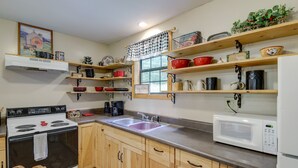 Een keuken met houten kastjes, een fornuis, een spoelbak en diverse keukengerei op planken.