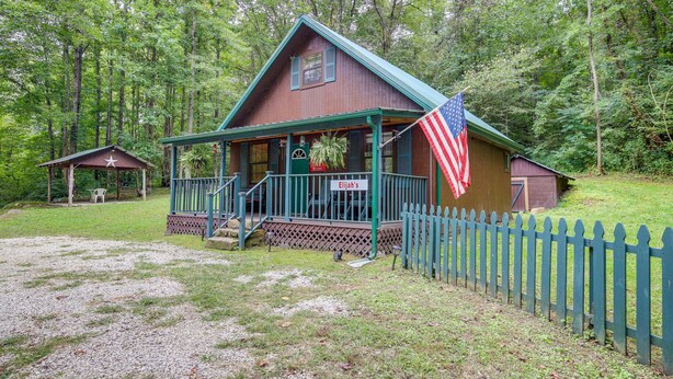 Een houten chalet met een veranda, een Amerikaanse vlag en een omheinde tuin.